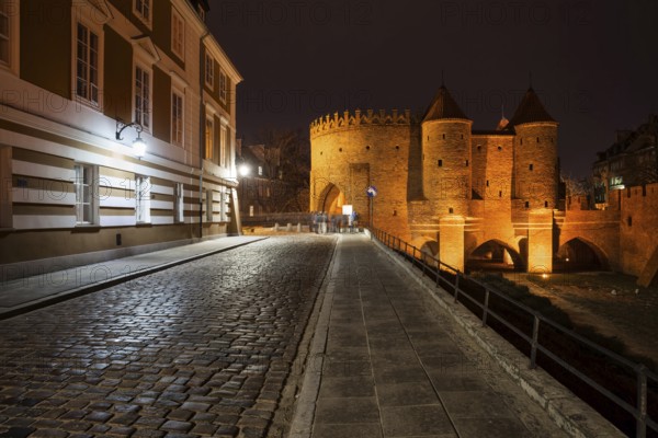 Cobblestone Podwale street and illuminated Barbican at night in city of Warsaw in Poland