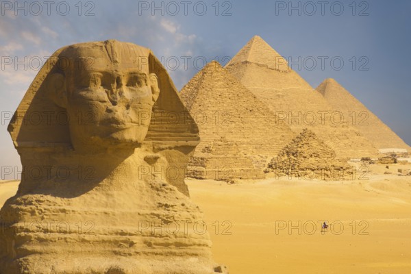 A closeup of the face of the Great Sphinx with a set of pyramids in the background on a beautiful clear blue sky day in Giza, Cairo, Egypt, Africa