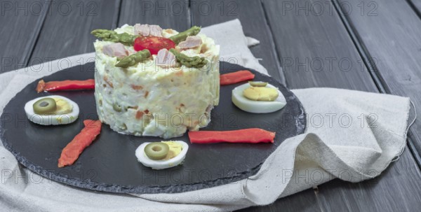 Black slate plate with ensaladilla rusa or Russian salad typical spanish tapa garnished with red bell pepper, hard boiled egg and asparagus