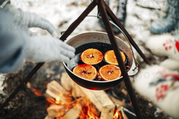 From above traditional mulled wine with slices of orange preparing in pot over burning logs in winter in countryside
