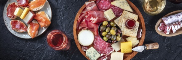 Italian antipasti or Spanish tapas panorama on a black background. Gourmet cold meat and cheese platter on a black background, shot from the top with wine. A variety of appetizers