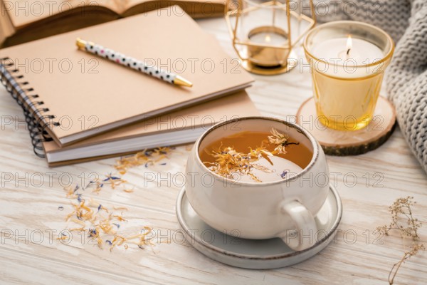 Hot herbal tea with notepad, candle, book and blanket. Cozy and hygge lifestyle
