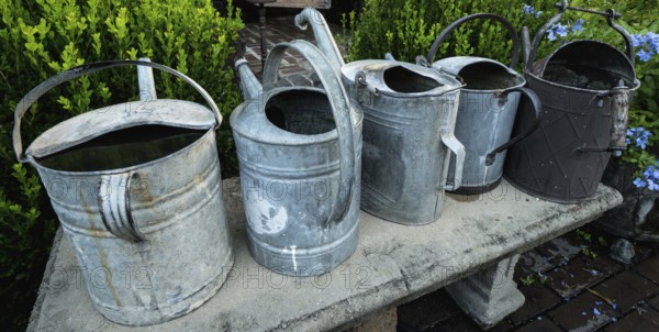 Several od rustic metal watering cans on a bench horizontal view
