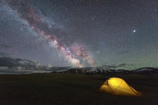 Milky Way on Starry Night Sky with Airglow and Yellow Glowing Tent. Camping Concept