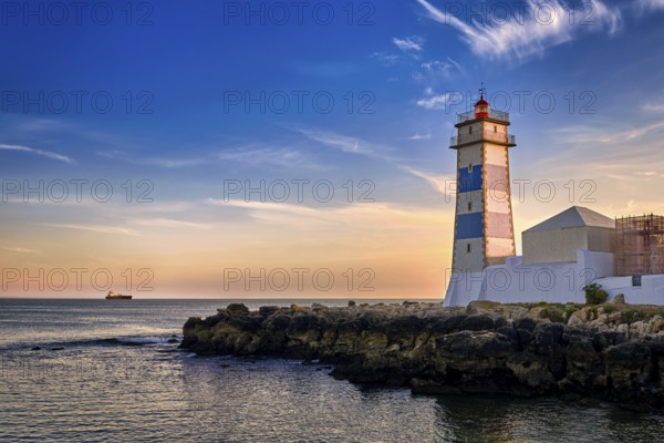 Dramatic sunset on sea shore and Santa Marta lighthouse in Cascais, Portugal. Colorful sky, clouds, sunlight, low sun, calm ocean waters, local landmark, safety and navigation tower, rocky shore