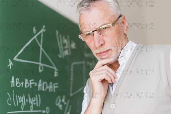 Aged professor standing near chalkboard classroom