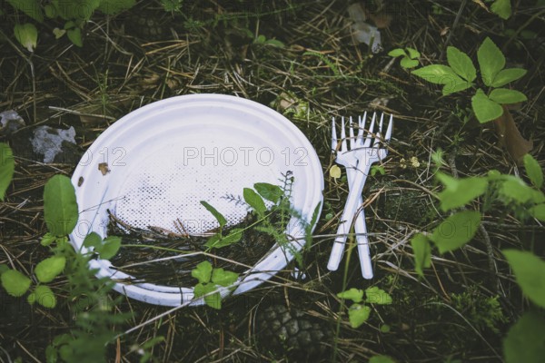 Plastic waste on the ground in forest, plate and fork left after a picnic