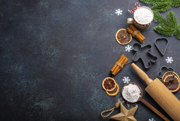 Christmas and New Year festive baking background with kitchen tools, flour, fir tree branch, metal cookie cutters on dark blue stone concrete background table top view, space for text frame