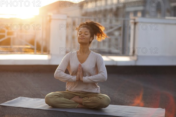 Cropped photo of woman sitting in lotus pose on mat and practicing yoga, female doing namaste gesture while meditating indoors. Meditation and mindfulness concept