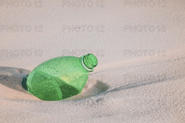 Green plastic bottle on sandy beach highlighting environmental pollution