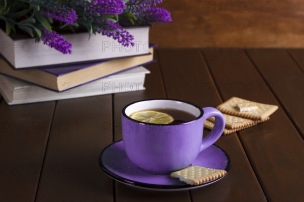 Cup of tea with lemon and cookies next to old books over vintage wooden background