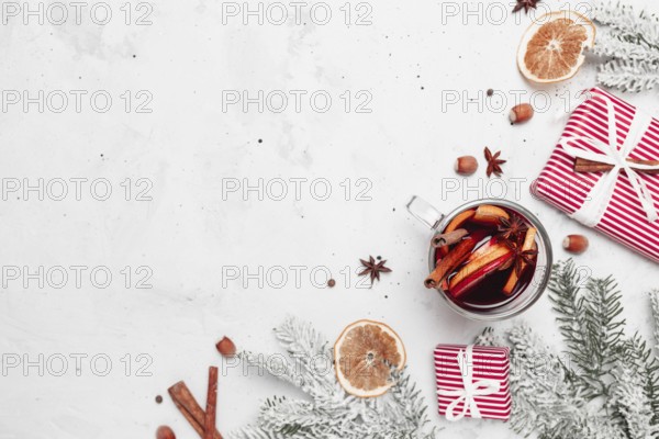 Christmas flat lay top view on white gray concrete background table with glass cup or mug of Mulled Wine, present red gift boxes, decorations, cinnamon sticks, hazelnut, dried or sublimated orange