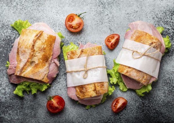 Fresh ciabatta sandwiches with ham, cheese, lettuce, tomatoes on stone concrete background, close-up, top view. Making healthy sandwiches for snack or lunch concept
