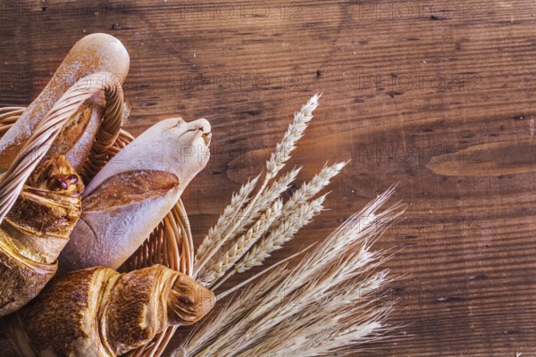 Close up view on baguettes and croissants in wicker basket with ears of wheat on old wooden boards horizontal version
