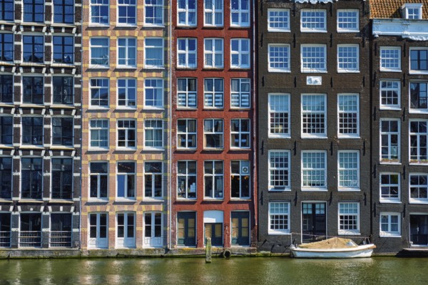 Row of typical houses and boat on Amsterdam canal Damrak with reflection. Amsterdam, Netherlands