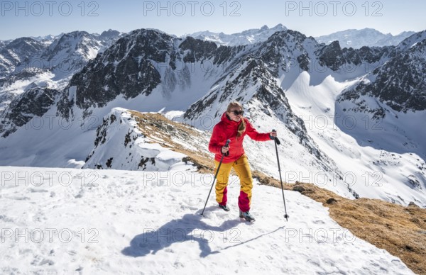 Ski tourer standing next to summit cross, summit of Mitterzeigerkogel in winter, Sellraintal, Kühtai, Tyrol, Austria, Europe