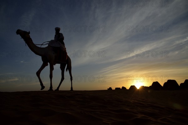 Man riding a camel at sunset at the pyramids of the north cemetery Meroe, Nubia, Nahr an-Nil, Sudan, Africa