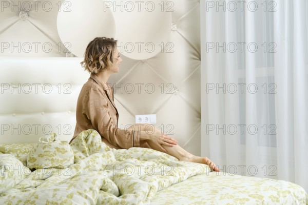 Joyful young woman sits on the bed and smiles