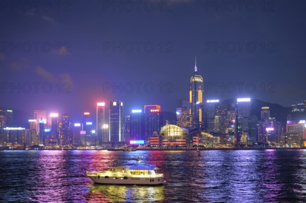 Hong Kong skyline cityscape downtown skyscrapers over Victoria Harbour in the evening illuminated with tourist boat ferries, Hong Kong, China, Asia
