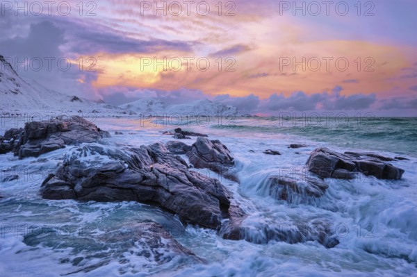Waves of Norwegian sea on rocky coast in fjord on sunset with sun. Skagsanden beach, Lofoten islands, Norway, Europe