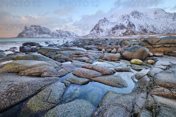 Rocks on beach of fjord of Norwegian sea in winteron sunset. Utakliev beach, Lofoten islands, Norway, Europe
