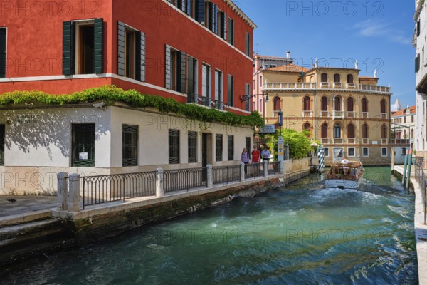 VENICE, ITALY, JULY 19, 2018: Narrow canal between colorful old houses with tourists in Venice, Italy, Europe