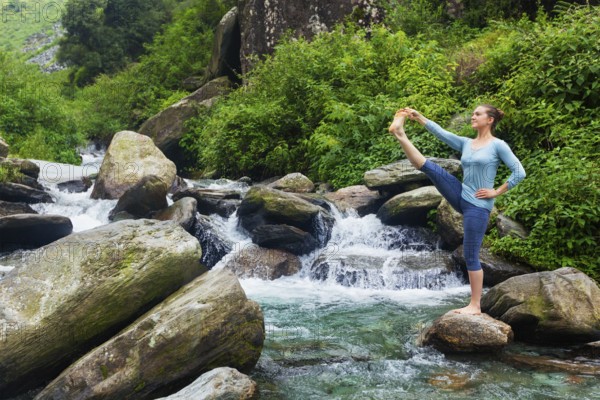 Yoga outdoors, woman doing Ashtanga Vinyasa Yoga balance asana Utthita Hasta Padangushthasana, Extended Hand-To-Big-Toe Pose position posture outdoors at waterfall