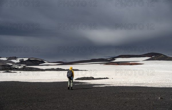 Hikers in snow-covered volcanic landscape with volcanic sand and petrified lava, crater of Askja volcano, Icelandic highlands, Iceland, Europe