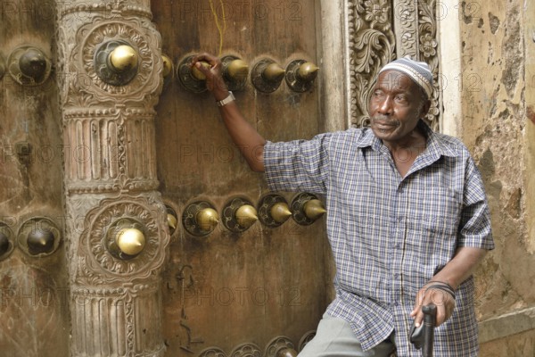 Elderly man leaning against a wooden door in the historic town centre, Zanzibar City, Zanzibar, Tanzania, Africa