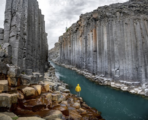 Tourist standing by the river in Stuðlagil Canyon, turquoise blue river between basalt columns, Egilsstadir, Iceland, Europe