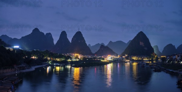 Panorama of Yangshuo town illuminated in the evening with dramatic karst mountain landscape in background over Li river. Yangshuo, China, Asia