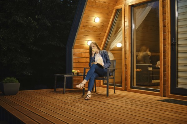 Late in the evening, a young woman sits on the terrace of a country house, eats an apple and reads a book