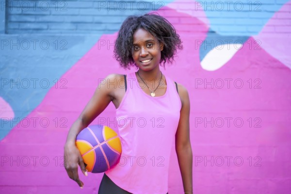 Portrait of a happy african female basketball player against colorful urban wall