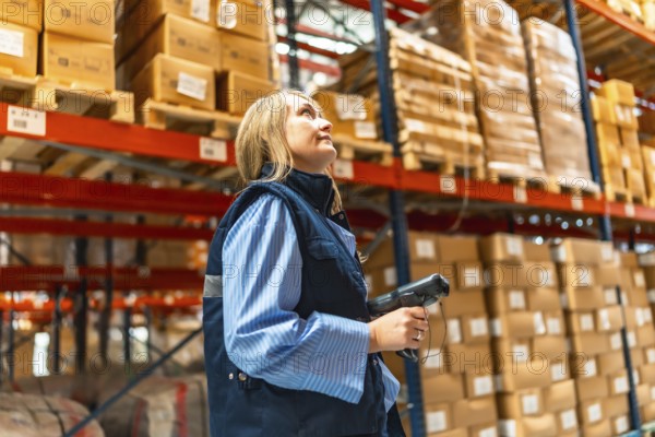 Blonde woman manual worker in waistcoat scanning parcels in a warehouse