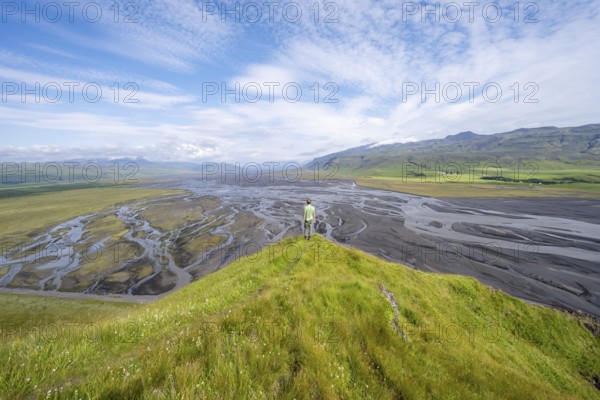 Hiker, young man on a hill, view over alluvial land, meandering river, Dímonarhellir, Suðurland, Iceland, Europe
