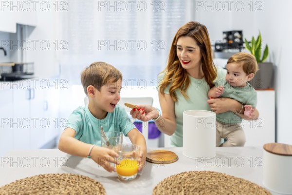 Happy woman feeding her son while holding a baby during breakfast at home
