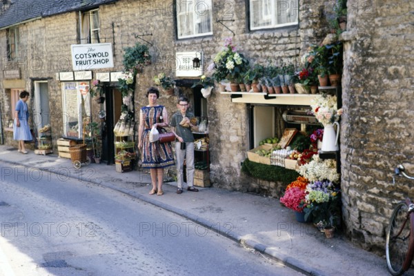 Stow on the Wold, Gloucestershire, England 1963 Woman and boy posing in front of a fruit shop in Cotswold