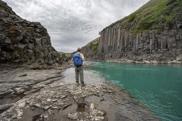Tourist standing by the river in Stuðlagil Canyon, turquoise blue river between basalt columns, Egilsstadir, Iceland, Europe