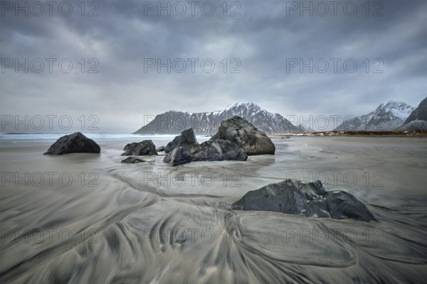 Rocks on beach of fjord of Norwegian sea in winter with snow. Skagsanden beach, Lofoten islands, Norway, Europe