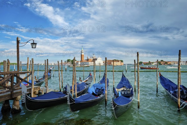 VENICE, ITALY, JUNE 27, 2018: Gondolas and gondolier in lagoon of Venice by Saint Mark (San Marco) square with San Giorgio di Maggiore church in background in Venice, Italy, Europe