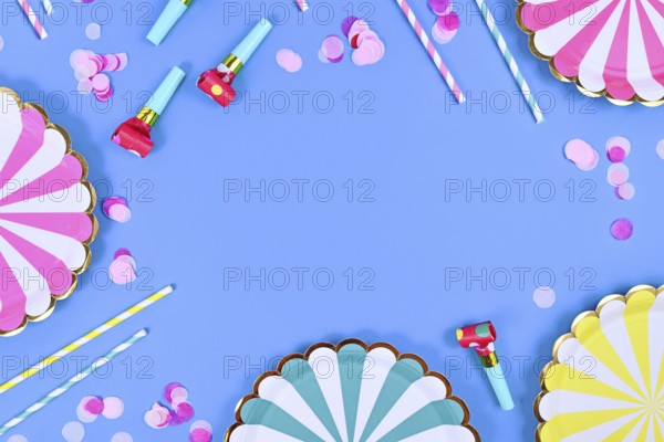 Party flat lay with paper plates, drinking straws and confetti on blue background with copy space