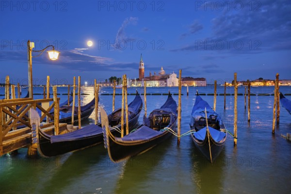 Romantic vacation Venice travel background, gondolas at Saint Mark (San Marco) square and Basilica San Giorgio Maggiore Church seen across Venice lagoon with full moon. Venice, Italy, Europe