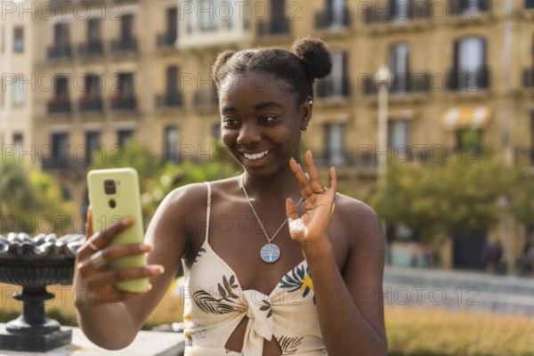 Young cute african woman waving during a video call with the mobile phone in the street