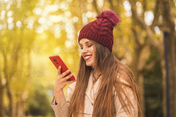 Portrait of a beautiful woman in autumn next to a forest in nature smiling sending a voice note with the phone