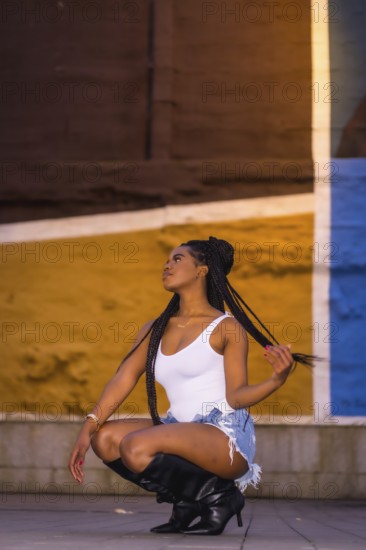Fashionable urban style with an African girl with braids on a street in the city at night. White shirt and pants, vertical photo