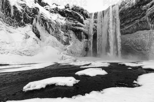 Skogafoss waterfall with icy and snowy rock face, black and white photo, Sudurland, Iceland, Europe