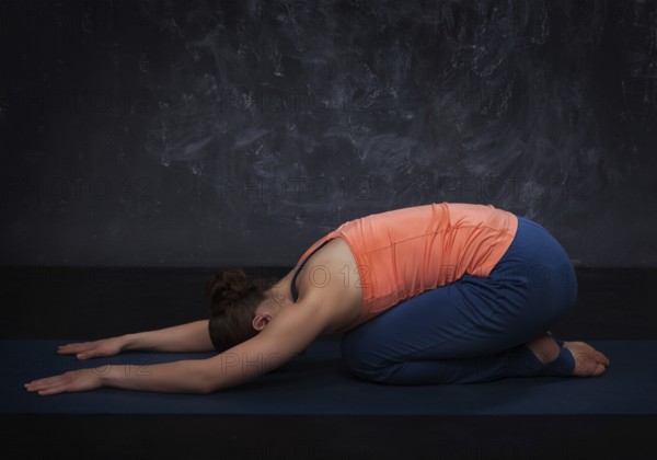 Beautiful sporty fit yogini woman practices yoga asana balasana (child's pose), resting pose or counter asana for many asanas on dark background