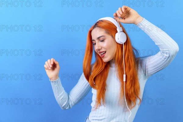 Redhead woman in studio photography smiling dancing on a blue background