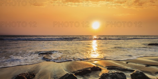 Tropical beach vacation background, panorama of waves and rocks on beach on sunset with beautiful cloudscape