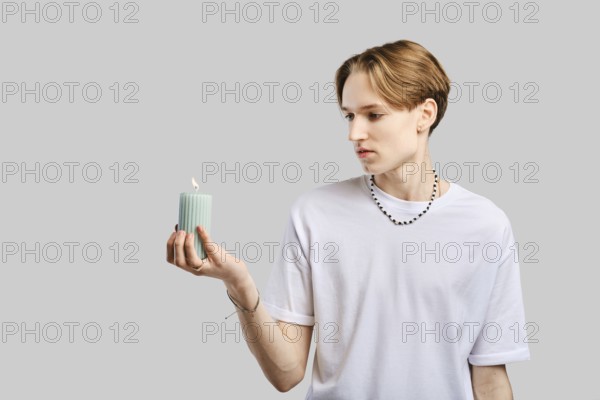 Young man holds candle in hand over grey studio background